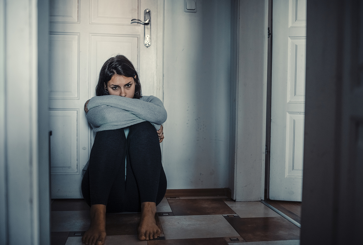 Young woman that struggles with mental disease is sitting desperately on the floor in the dark room