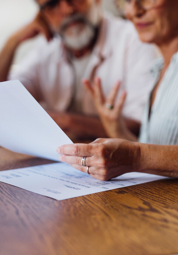 A senior couple is seen reviewing important documents together at home, emphasizing careful consideration and financial planning.